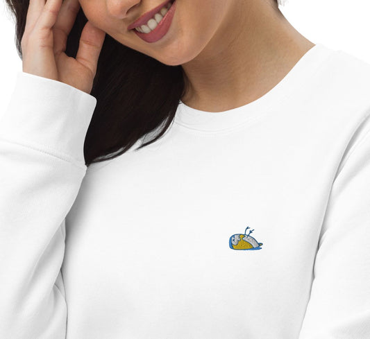 Close-up of a woman displaying a white sweater, Thoughtful. The sweater has a multi-coloured sparrow embroidered on the left side of the t-shirt.