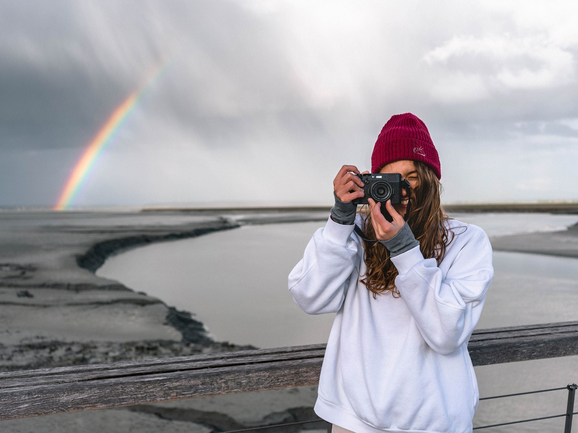 Close-up of a woman taking photographs. She is wearing a burgundy cap with the DEAD s