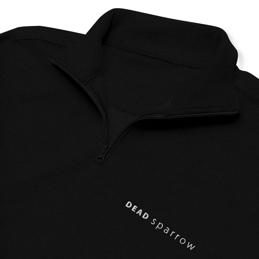 Detail image of a black zip up sweater for women. The image shows a close-up of the zipper and logo. Product name Outstanding.