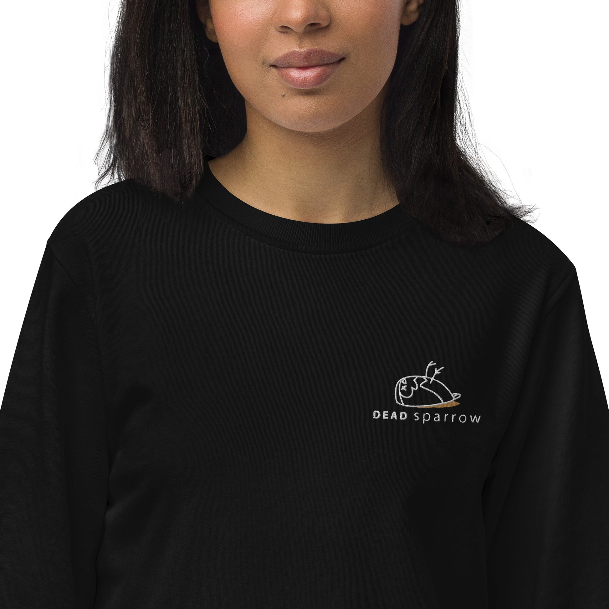 Close-up of a woman wearing an organic sweatshirt in the colour black. DEADsparrow logo embroidered on the left side in white and gold. Product name Significant. Significant is made from organic cotton and recycled materials.