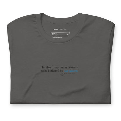 Image of a Survivor t-shirt for women. In the picture, the t-shirt is folded and has the colour dark grey. The t-shirt has the quote "Survived too many storms to be bothered by raindrops". DEADsparrow.store.