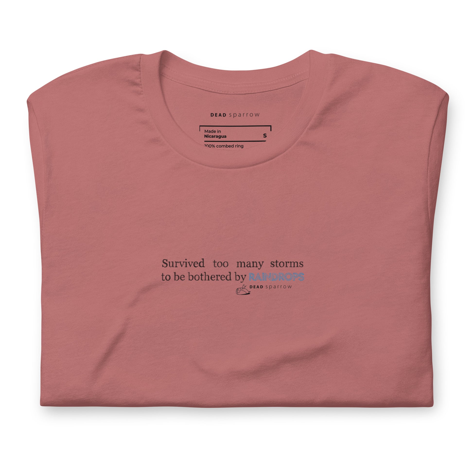 Image of a Survivor t-shirt for women. In the picture, the t-shirt is folded and has the colour mauve. The t-shirt has the quote "Survived too many storms to be bothered by raindrops". DEADsparrow.store.