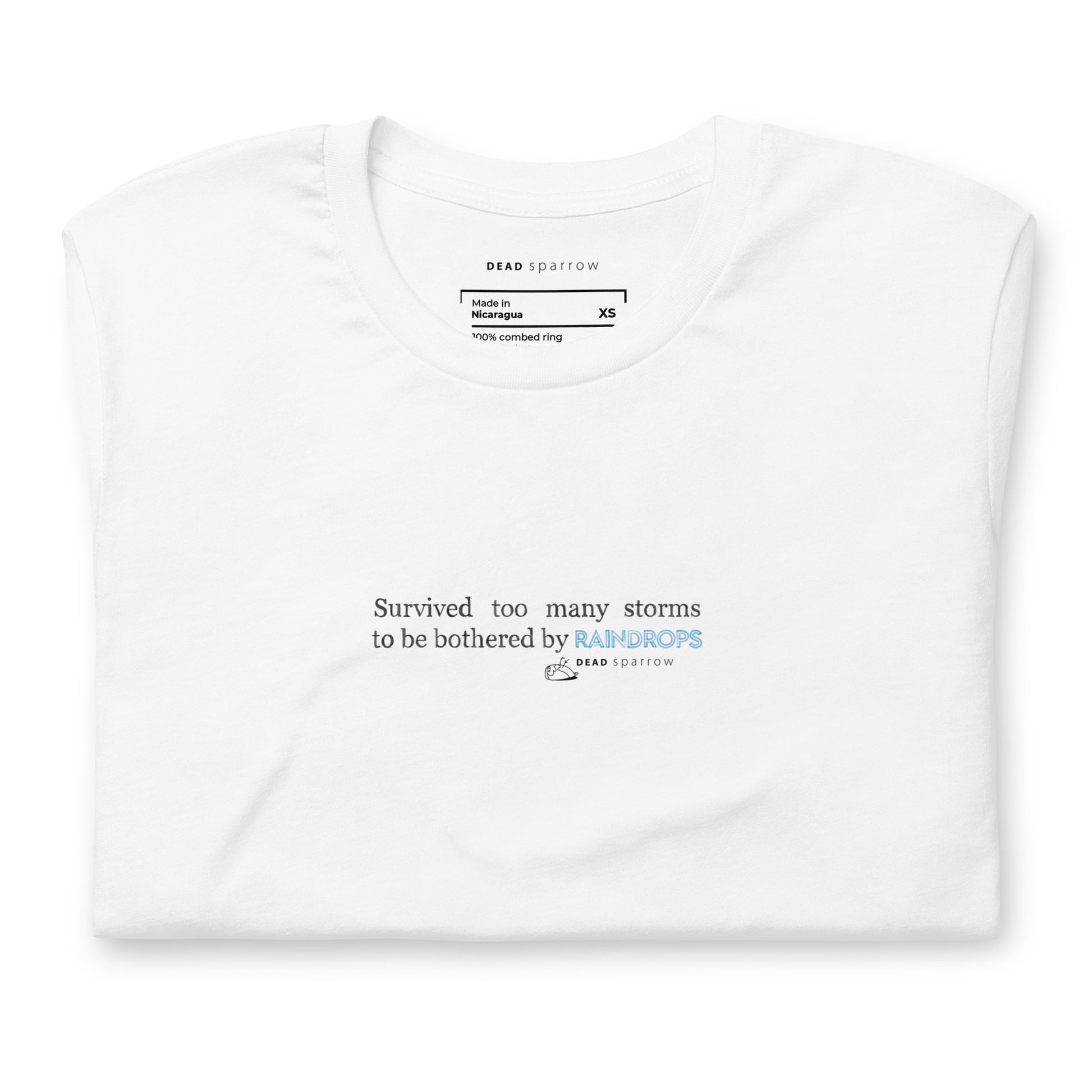 Image of a Survivor t-shirt for women. In the picture, the t-shirt is folded and has the colour white. The t-shirt has the quote "Survived too many storms to be bothered by raindrops". DEADsparrow.store.