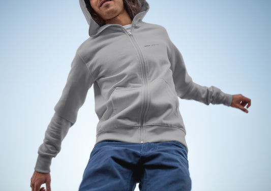 Close-up of a man wearing a light grey zip-up hoodie, item name Observent. The hoodie has a print on the left side, 'DEAD sparrow' (logo).